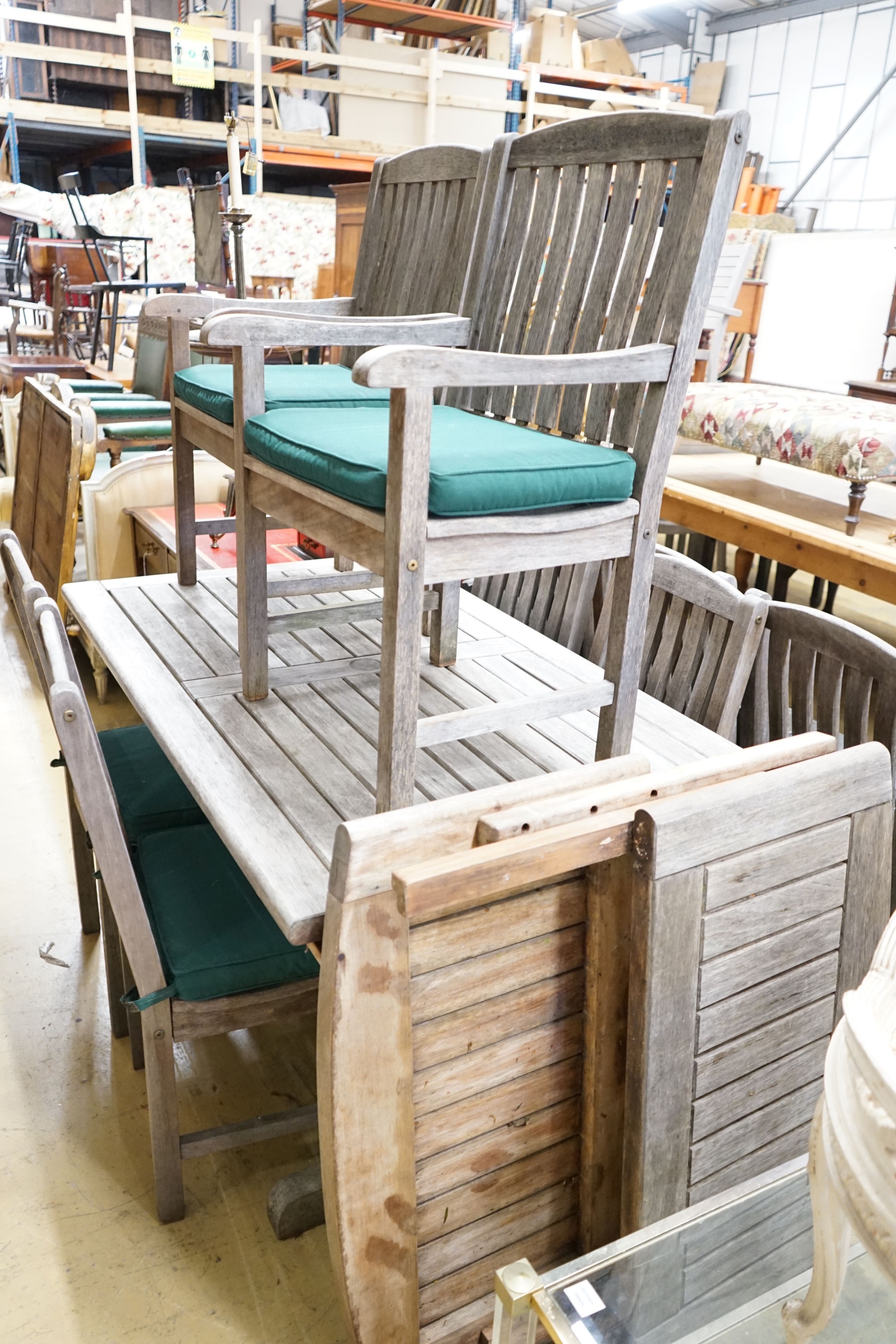 A rectangular weathered teak garden table with removable end sections, together with ten garden chairs, with seat pads, two with arms